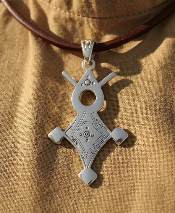 Pendentif croix touareg en argent porté sur cordon de cuir avec motifs géométriques traditionnels africains.